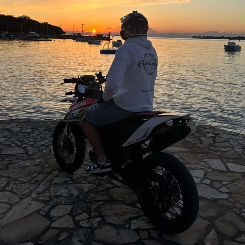 Sonnenuntergang am Hafen, Motorradfahrer im INFA 295 ONE LOVE Hoodie, steht mit dem Rücken zur Kamera. 