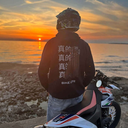 Person im INFA 295 BIKELIFE Hoodie sitzt bei Sonnenuntergang am Meer auf einem Motorrad.