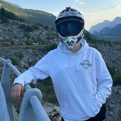 Motorradfahrerin im INFA 295 ONE LOVE Hoodie mit Motocross-Helm, stehend an einem Geländer in einer Berglandschaft.