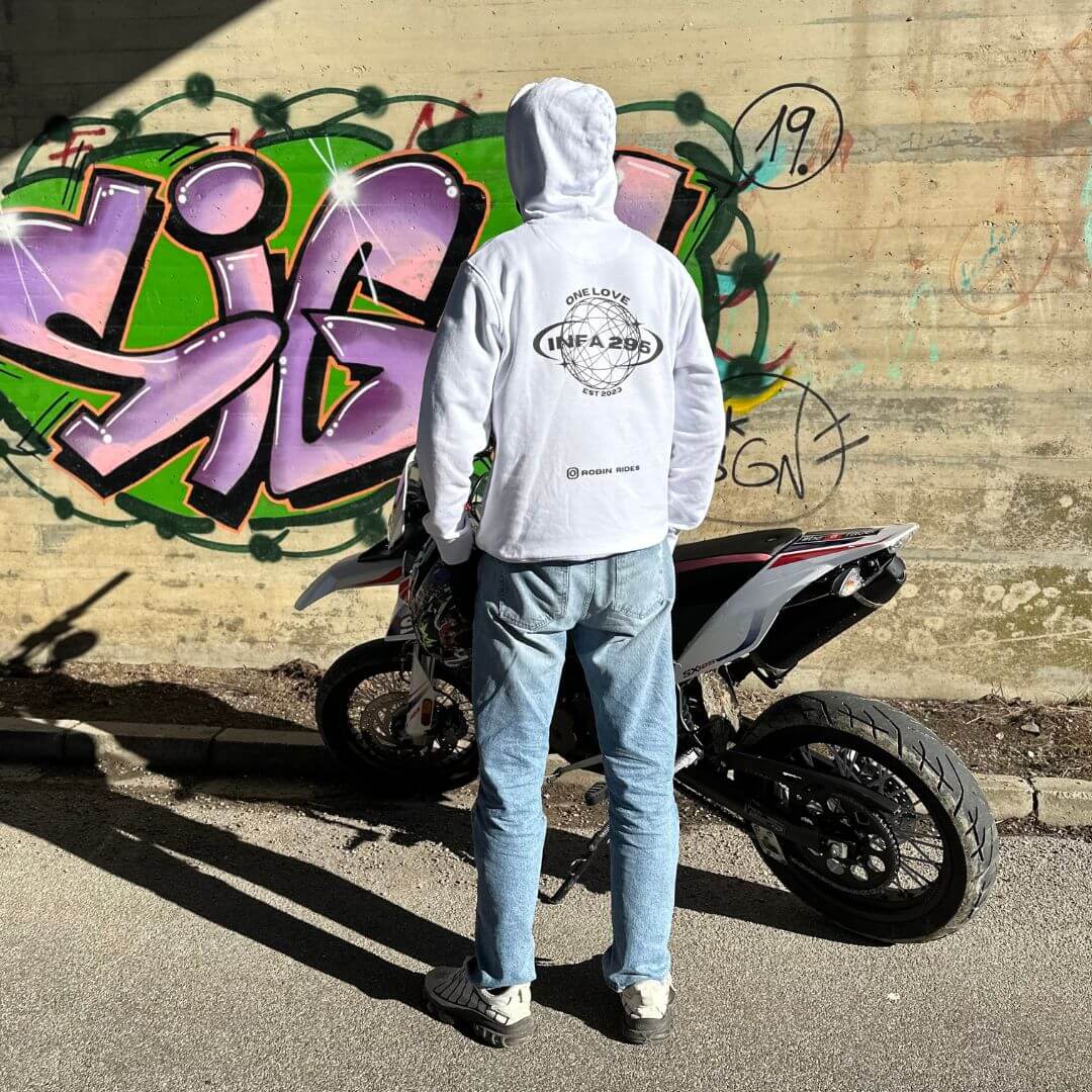 Person im INFA 295 ONE LOVE Hoodie steht neben einem Motorrad vor bunter Graffiti-Wand.