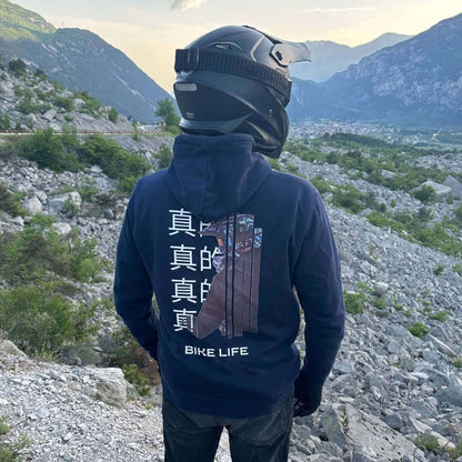 Motorradfahrer im INFA 295 Bike Life Hoodie mit Rückenprint, stehend in einer felsigen Berglandschaft.