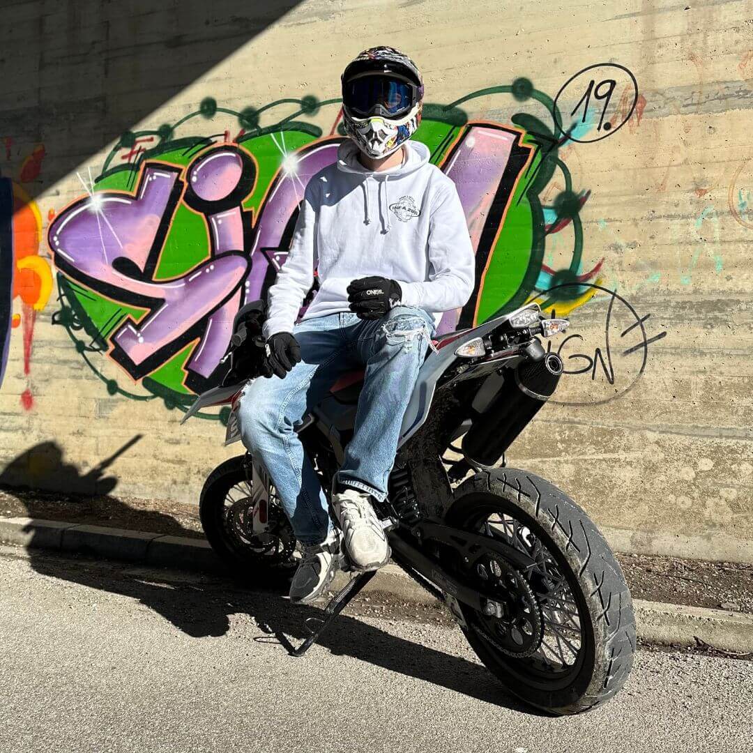 Motorradfahrer im INFA 295 ONE LOVE Hoodie sitzt auf einem Motorrad vor einer lebhaften Graffiti-Wand.